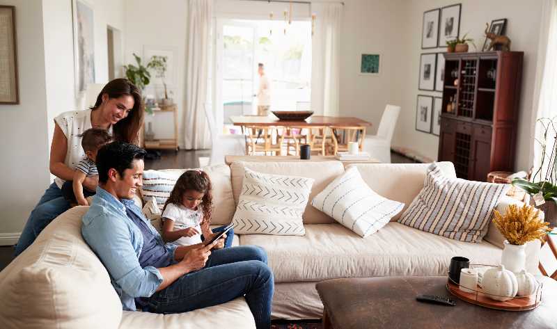 Family of four relaxing together on a bright living-room sofa, illustrating year-round home comfort.