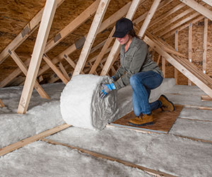 Worker installing white fiberglass in an attic floor.