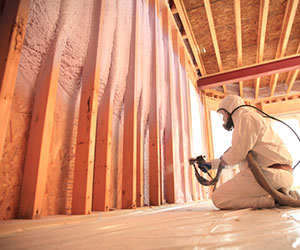 Worker in a white safety suit installing spray foam insulation.