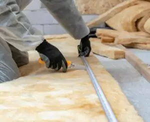 Insulation installer measuring and cutting fiberglass batt insulation.