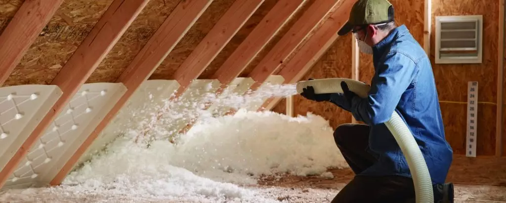 Man installing blown in fiberglass inside an attic