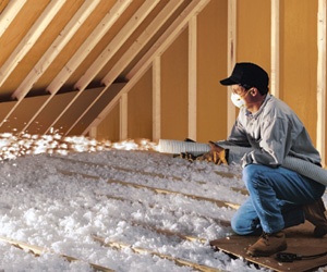 Worker installing blown-in fiberglass insulation in an attic.