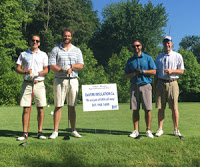 Four golfers standing next to a sign on a golf course.